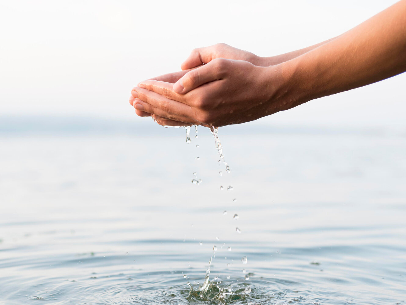Mains recueillant de l'eau claire au-dessus d'une étendue d'eau